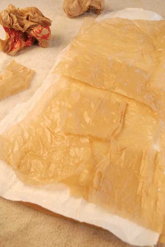 Lay two or more sheets of white bag so they overlap by a couple inches, creating a one-layer base that’s 14 by 36 inches. Stack pieces until base is three layers deep. Cover with parchment and iron from center outward so plastic fuses—30 to 60 seconds. Let cool. Add a fourth layer and iron so finished “fabric” is four layers thick. Flip and iron other side. If fabric is not fully laminated, iron again.